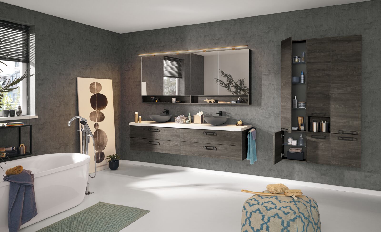 Badkamer met links een vrijstaand bad, in het midden een wasmeubel met twee opzetwastafels in een natuurstenen materiaal met zwarte kranen.